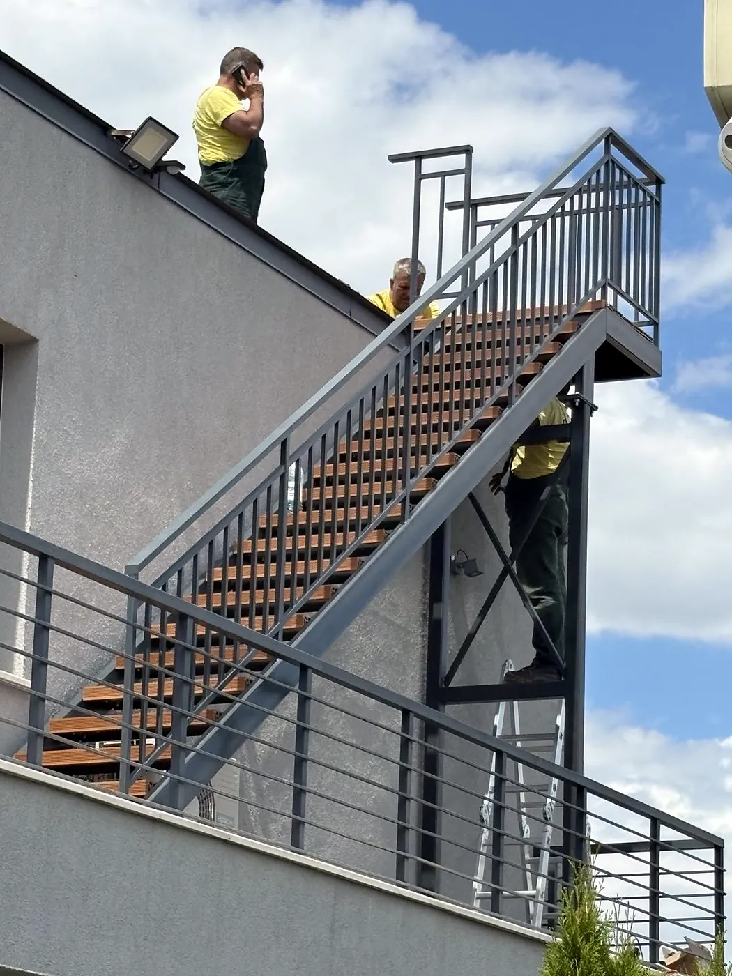Außentreppe aus Stahl mit Holzstufen und senkrechtem Stabgeländer, an einem Gebäude montiert