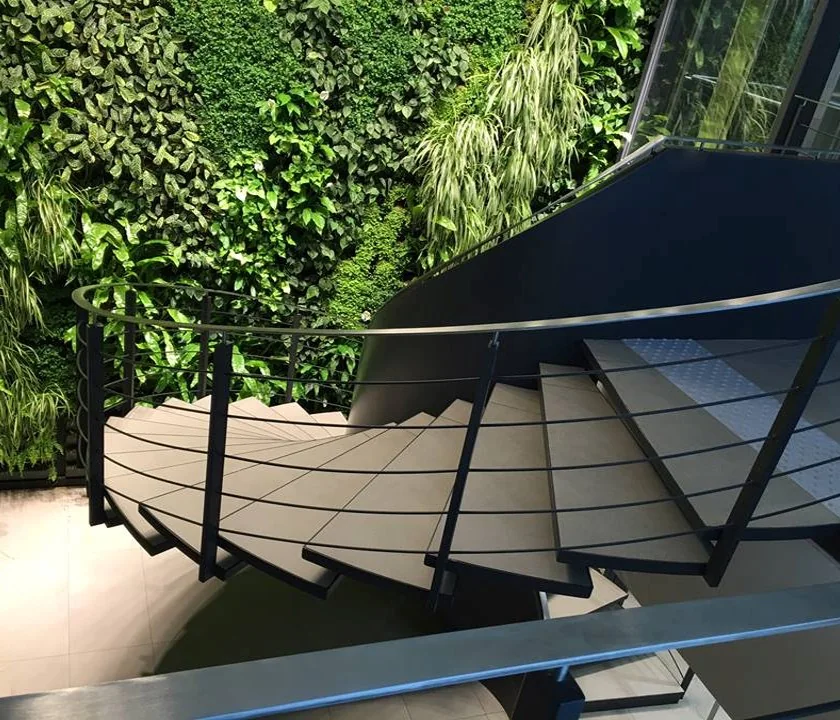Stahl-Wendeltreppe mit Holzstufen und Seilgeländer vor einer Pflanzenwand